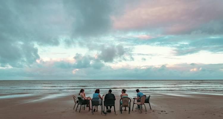 Group of people sitting on chairs on a peaceful beach at sunset.