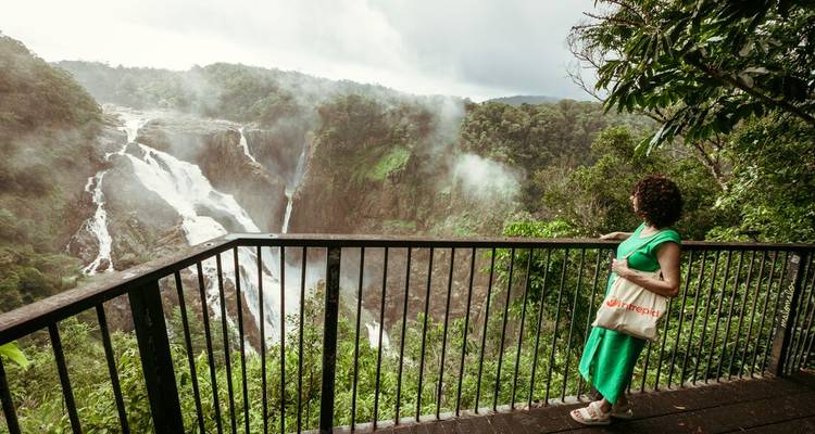 Traveller in green dress admires a thundering rainforest waterfall from a viewing deck.