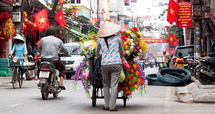 Straatbeeld met een verkoper die een karretje duwt met kleurrijke bloemen en Vietnamese vlaggen.