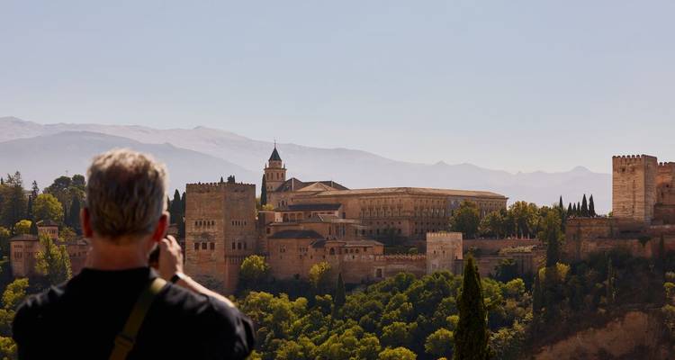 Un fotógrafo captura una vista panorámica del complejo palaciego de la Alhambra enclavado en colinas verdes.