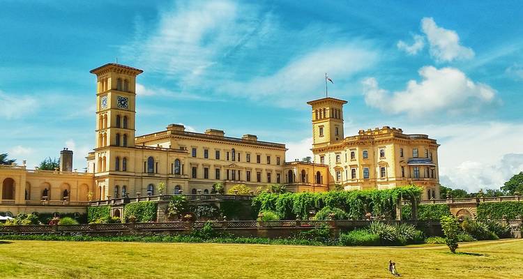 Palais d'époque victorienne avec deux tours d'horloge jumelles et jardins luxuriants sous un ciel bleu éclatant