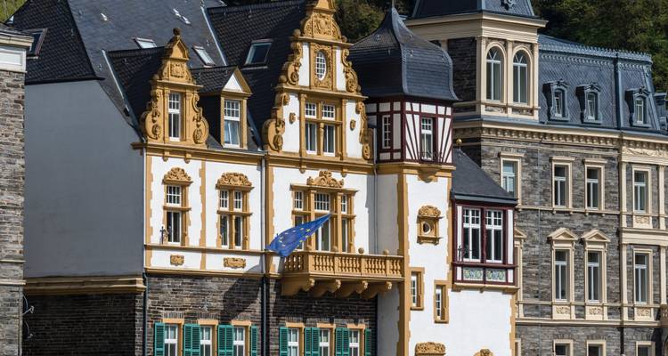 Elegant historic buildings with ornate façades line a riverside street in a Rhine town.