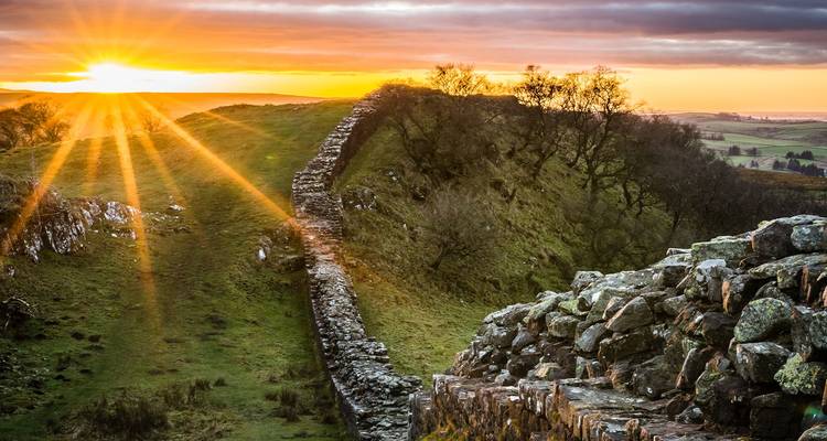 Der goldene Sonnenaufgang erhellt Hadrians Wall, der sich über sanfte Hügel erstreckt.