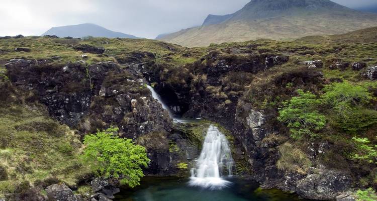 Pequeña cascada en cascada que se desploma en una piscina cristalina rodeada de colinas escarpadas en la Isla de Skye.