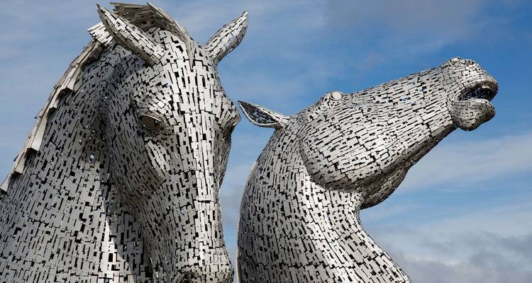 Primer plano de las imponentes esculturas de cabezas de caballo Kelpies metálicas recortadas contra un cielo azul.