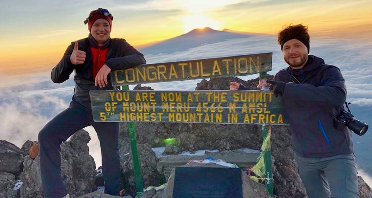 Zwei Wanderer posieren mit einem Schild auf dem Gipfel des Mount Meru.