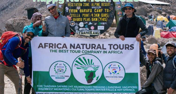Wandelaars poseren met een toerbanner voor een Kilimanjaro-kampteken te midden van rotsachtig alpijn terrein