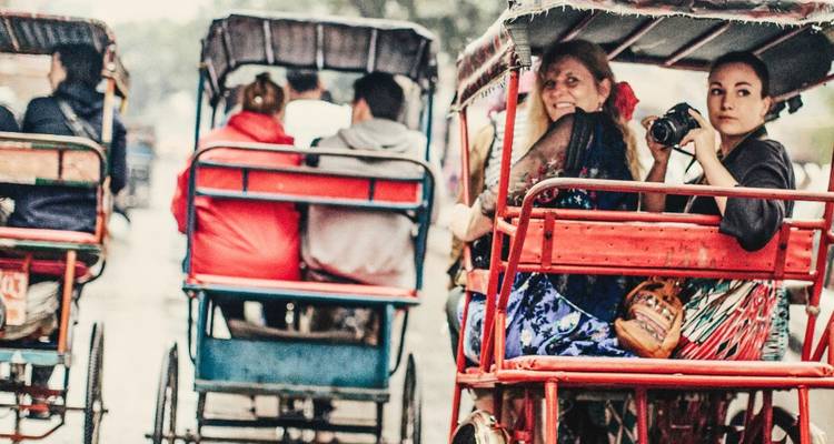 Viajeros montando en coloridos tuk-tuks de ciclo por una calle concurrida bajo la lluvia