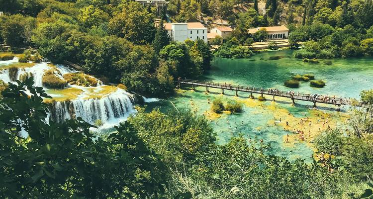 Vue aérienne des chutes d'eau, des bassins et du pont à pied envahis de nageurs au Parc national de Krka.