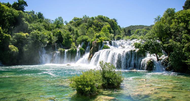 Les puissantes cascades de la chute d'eau de Krka se jetant dans un bassin d'eau émeraude entouré d'une végétation luxuriante.