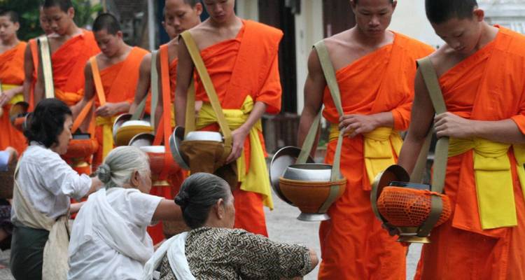 Monks in traditional attire receiving alms in a procession.