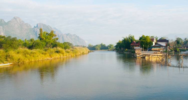 Calm river winding past greenery and mountains with a small village on the bank.
