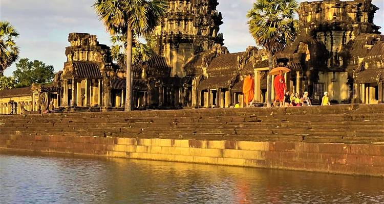 Mönche, die entlang eines alten Tempels neben einem Gewässer wandeln.