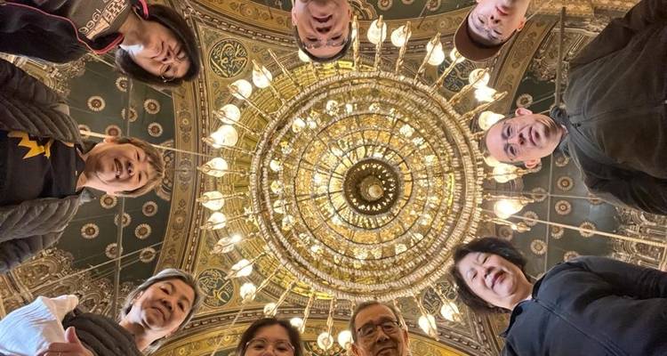 People standing in a circle looking up at a beautifully detailed ceiling with ornate designs.