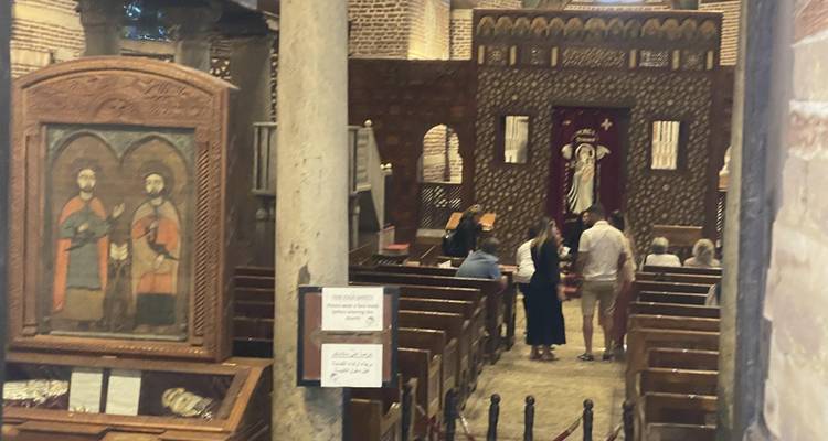 Interior of a church with people sitting in wooden pews near ornate decorations.
