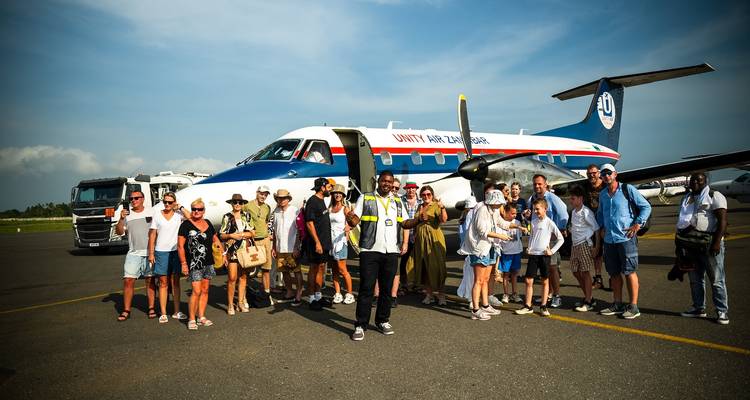 Group of people posing in front of a small airplane.