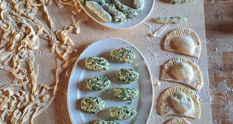 Mesa rústica cubierta con ñoquis de espinaca hechos a mano, ravioles y cintas de pasta fresca espolvoreadas con harina.