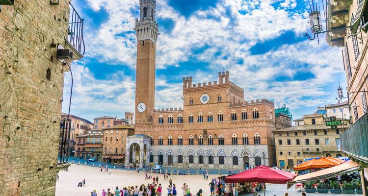 Plaza del Campo llena de vida en Siena con multitudes y la alta Torre del Mangia bajo un cielo radiante.