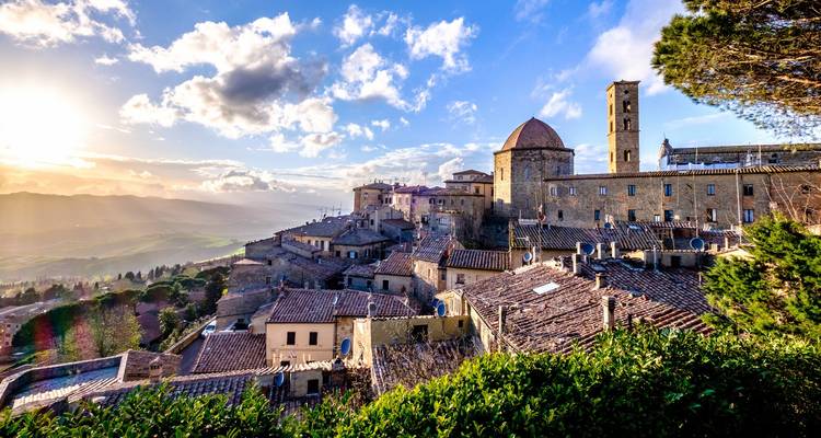 La luz del atardecer baña el pueblo medieval en la cima de la colina de Volterra y las colinas ondulantes de la Toscana.