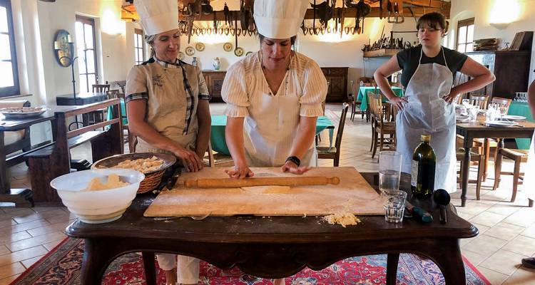 Los participantes con sombreros de chef estiran la masa de pasta en una tabla de madera durante una clase de cocina rústica.