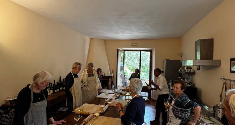 Un pequeño grupo de viajeros se reúne alrededor de estaciones de trabajo para una clase de elaboración de pasta en una acogedora cocina.