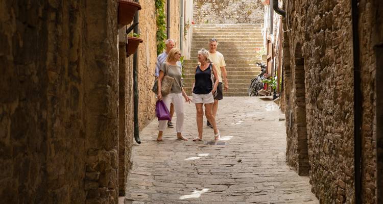 Les voyageurs se promènent dans une ruelle pavée étroite entre des bâtiments en pierre dans une charmante ville médiévale.