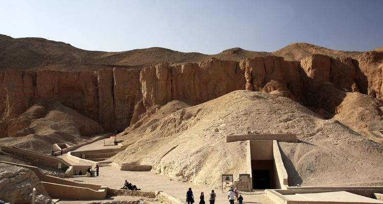 Paisaje de valle con turistas caminando hacia las entradas de las tumbas.