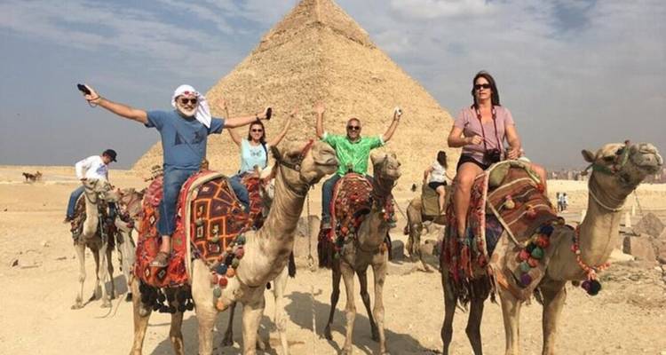 Tourists riding camels in front of a pyramid.