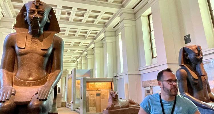 Indoor museum setting with ancient Egyptian statues and a man observing them.