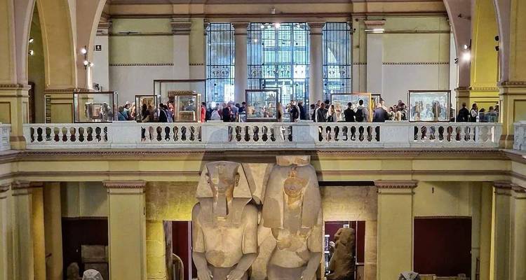 Museum interior with large statues and crowd of people on upper level.