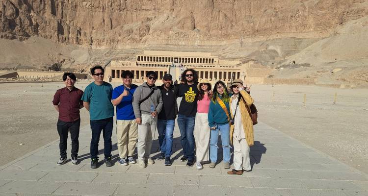 Touristen stehen vor dem Deir el-Bahri Tempel mit einer Bergkulisse.