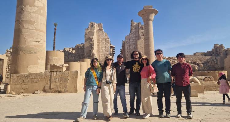 Groupe de touristes posant devant des ruines antiques avec des colonnes et un ciel bleu.