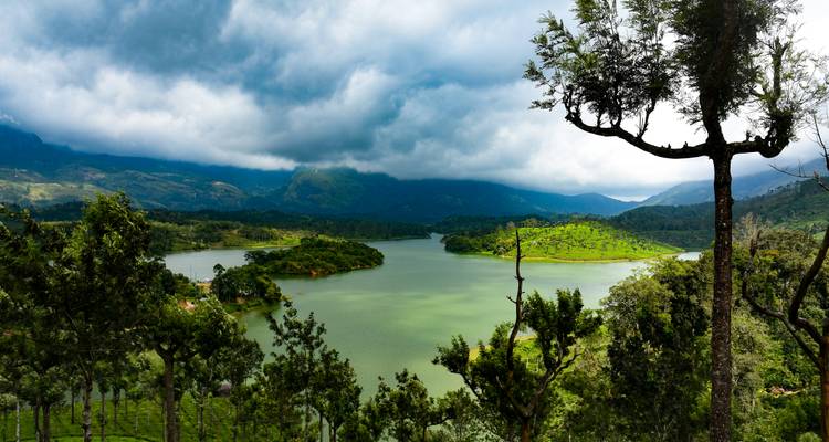 Scenic lake surrounded by green hills and dramatic monsoon clouds in Kerala.