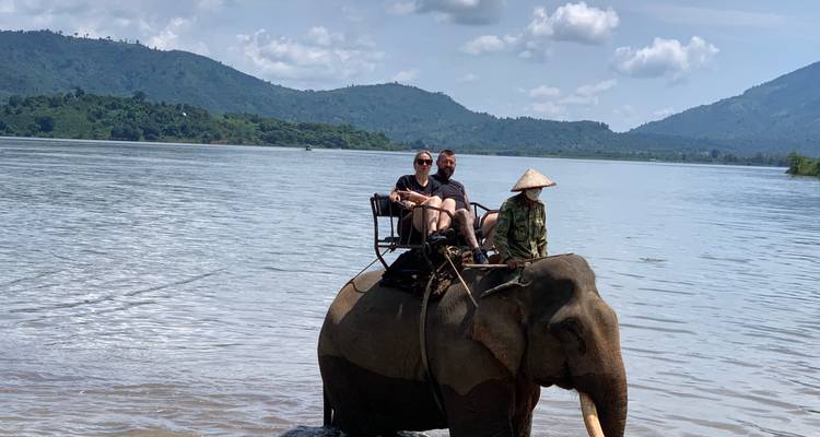 Des gens montant un éléphant dans une rivière avec des montagnes en arrière-plan.