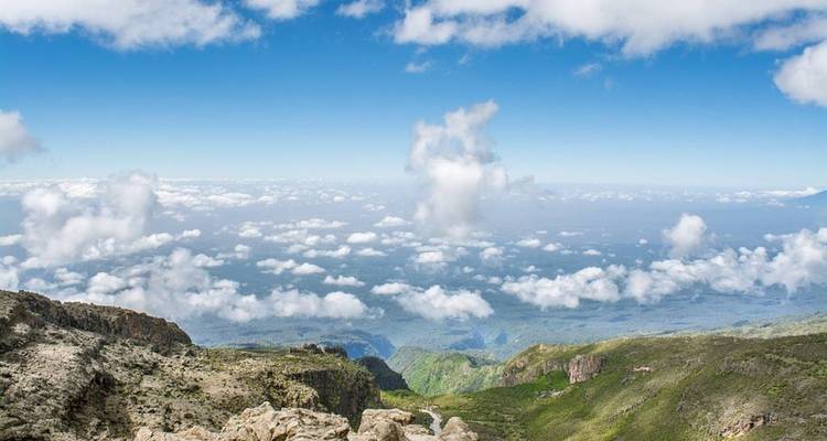 Vue depuis une montagne sur un vaste paysage avec des nuages.