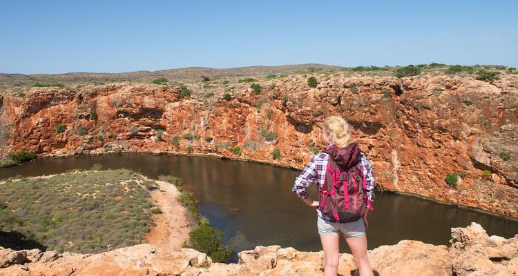 Excursionista mujer con una mochila de pie en el borde de un cañón de rocas rojas mirando un río sinuoso