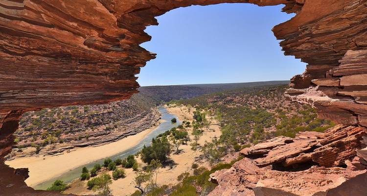 Icónico arco de roca enmarcando un amplio valle de río desértico con acantilados rojos estratificados bajo un cielo azul despejado