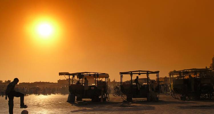 Silhouet van mensen en marktkramen bij zonsondergang op een groot open plein.