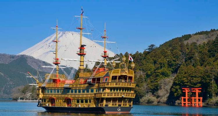 Ein golden glänzendes Piratenschiff im Kreuzfahrtstil segelt an einem Torii-Tor am Seeufer vorbei, während der Berg Fuji majestätisch dahinter aufragt.
