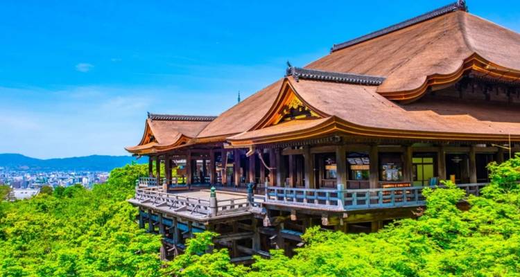 Kiyomizu-dera-Tempel umgeben von Grün, mit einem strahlend blauen Himmel.