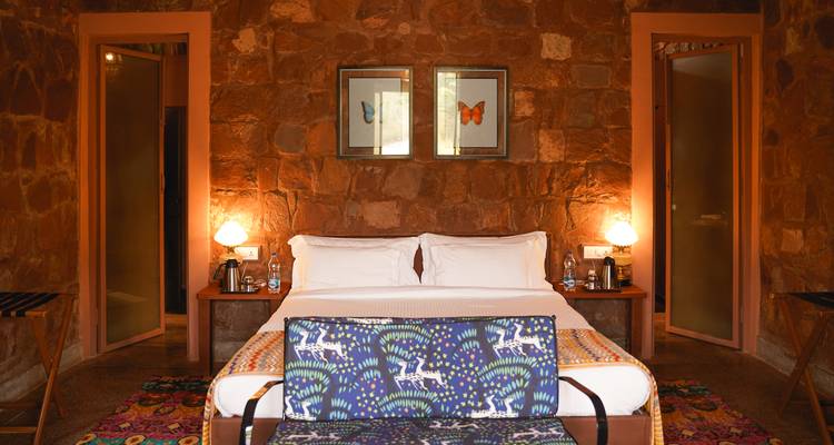 Acogedora habitación de lodge boutique con iluminación cálida, paredes de piedra, textiles estampados y lámparas de mesita de noche.