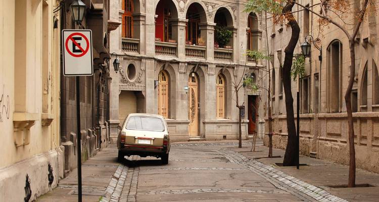 Callejón de piedra flanqueado por una arquitectura colonial ornamentada y un auto antiguo estacionado.