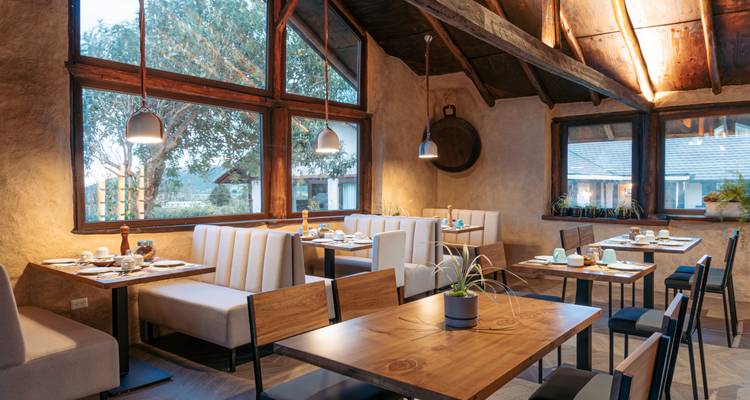 Heldere, moderne restaurantruimte met grote ramen die uitkijken op tuincottages.