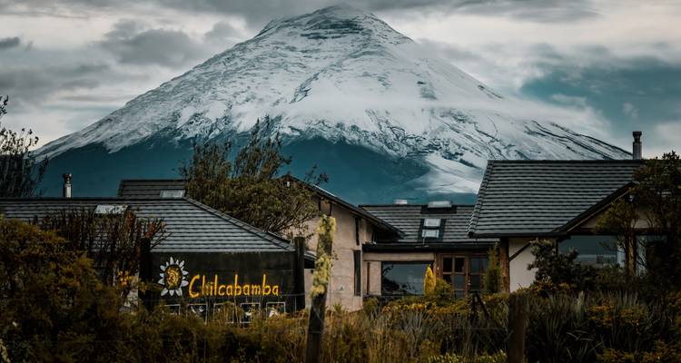 Berghuiscomplex onder de dramatische sneeuwbedekte Cotopaxi-vulkaan onder somber uitziende lucht.