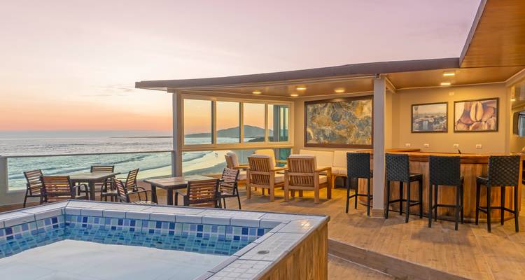 Terrasse sur le toit avec piscine, bar et vue sur le coucher de soleil océanique dans un hôtel de plage moderne.