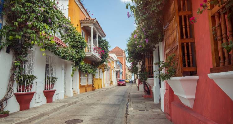 Calle tranquila bordeada de flores con fachadas coloridas y balcones en el barrio histórico de Cartagena.