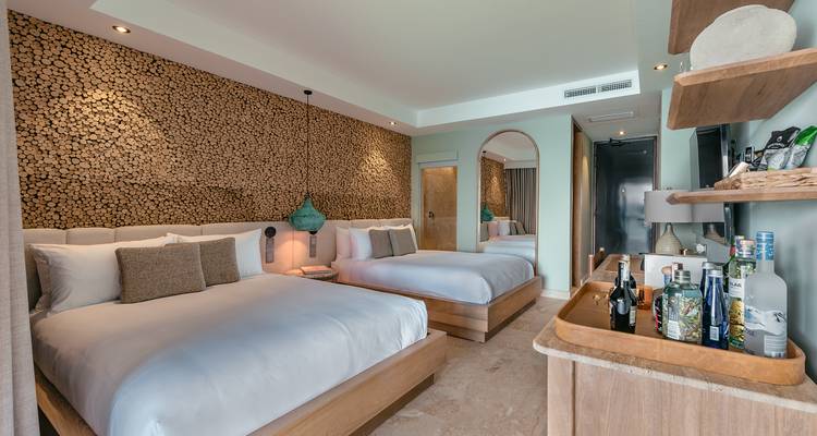 Habitación de hotel moderna con dos camas king, detalles de madera y minibar surtido.