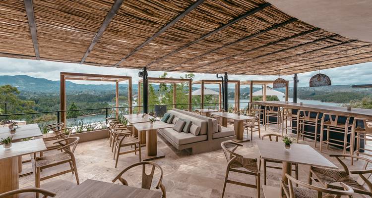 Terraza de restaurante al aire libre con estilo que ofrece vistas a un enorme lago y montañas ondulantes.