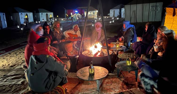 Grupo de personas sentadas alrededor de una fogata por la noche en un campamento del desierto.
