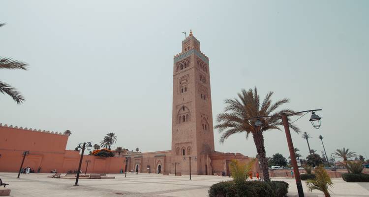 Hoher Minarett in einem Innenhof mit Palmen.